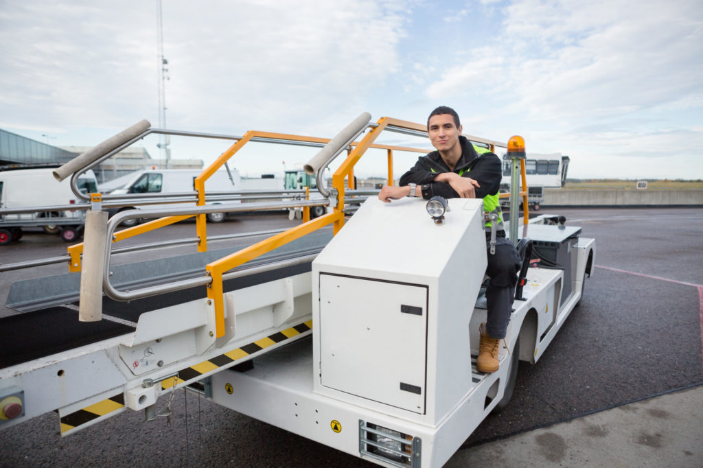 Portrait of confident worker sitting on luggage conveyor truck at airport
