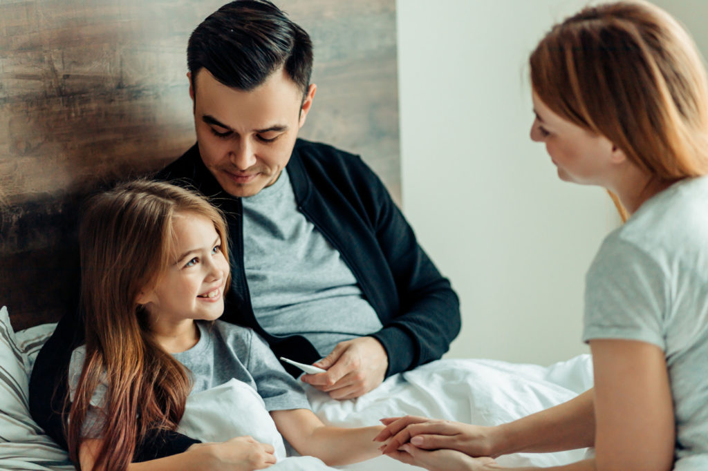 sweet careful family take care of sick daughter on bed, smiling caucasian family at home treating ill kid girl. family concept