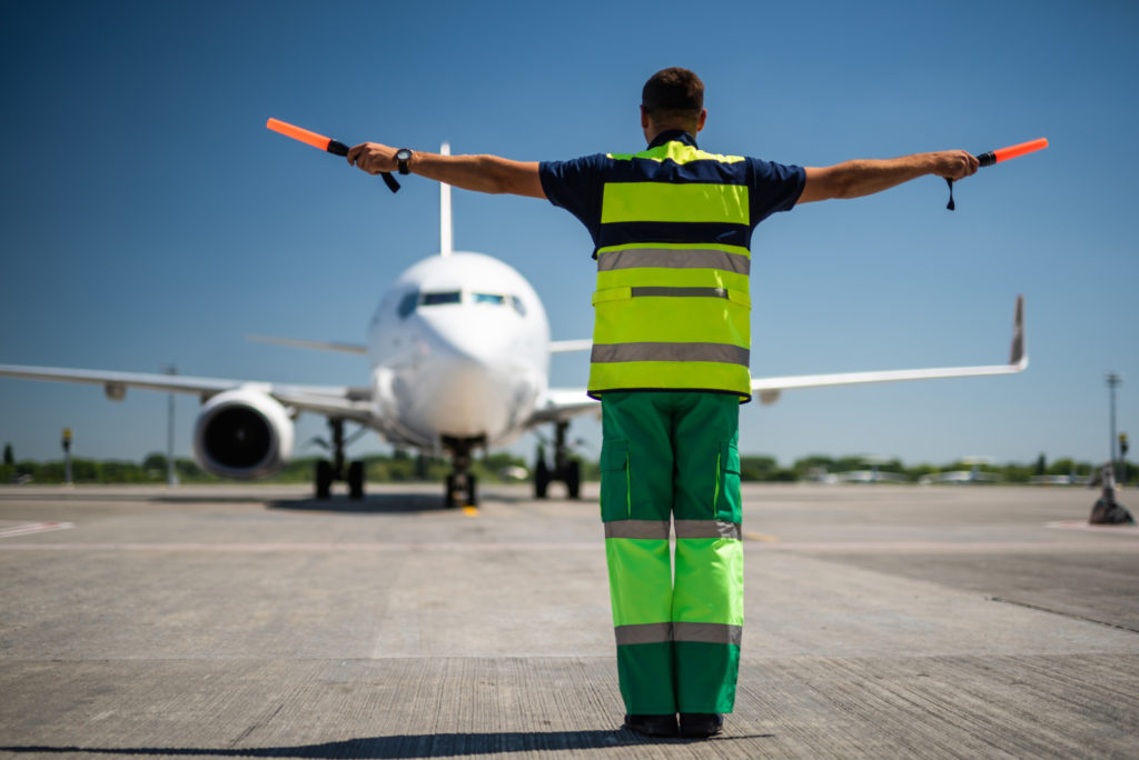 Welcome back. Back view of airport worker looking at passenger plane and signaling