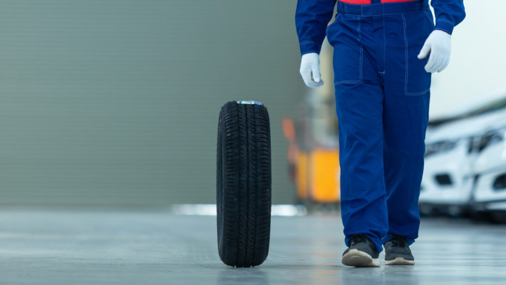 Auto mechanic change tire attractive auto mechanic man in blue uniform with blue gloves rolling wheel going on the autoservice in the auto repair center