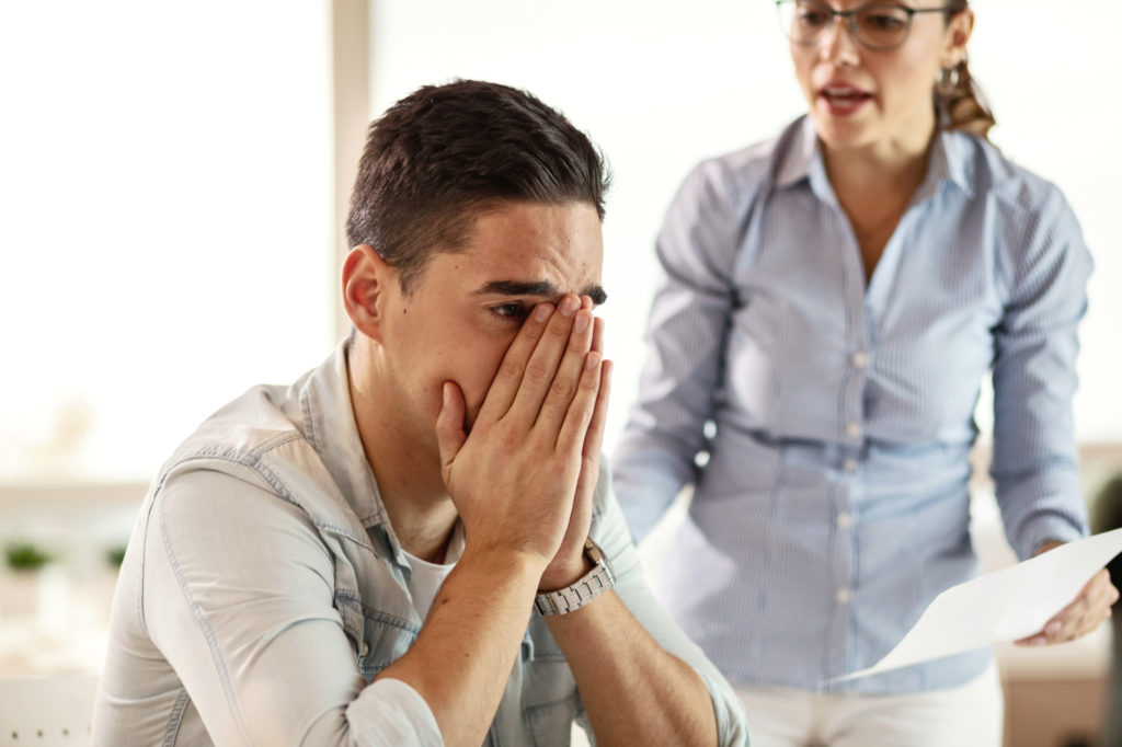 Stressed businessman feeling sad while his female boss is scolding him at work.