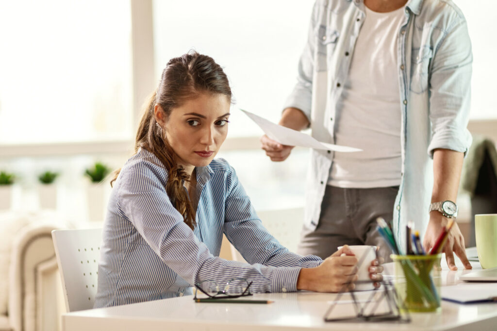 Young businesswoman looking away and thinking while her boss is scolding her at work.