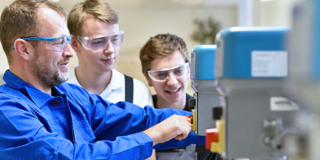 Group of young people in mechanical vocational training with teacher at drilling machine