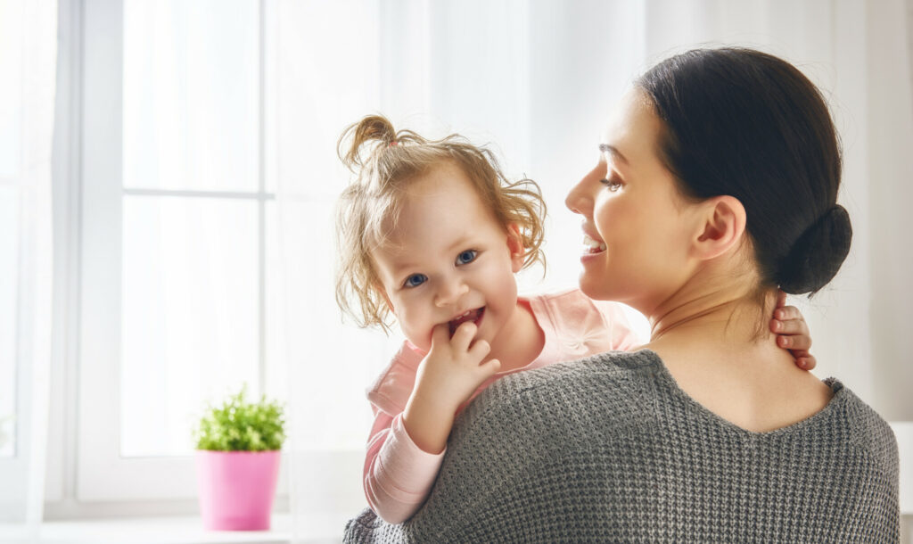 Happy loving family. Young mother are playing with her baby girl in the bedroom. Mom and child are having fun together.