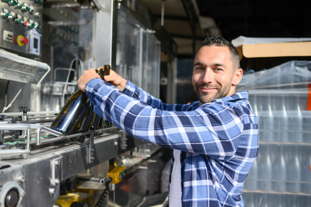 young man wine maker working filling wine bottle with automatic bottling machine