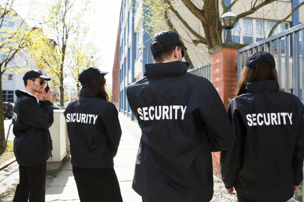 Rear View Of Security Guards In Black Uniform Standing Outside Building