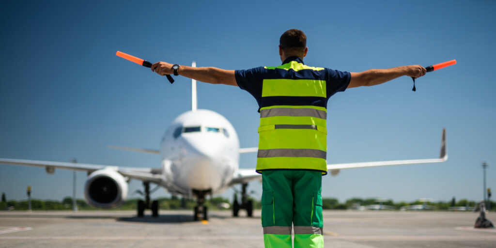 Welcome back. Back view of airport worker looking at passenger plane and signaling